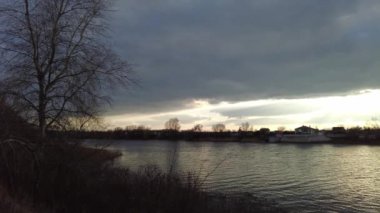 Nehirde gün batımı olan manzara. Bulutların arasından geçen güneş. Güneş ve su ışınları. Akşam yağmurlu manzarası.