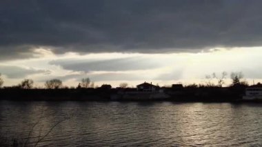 Nehirde gün batımı olan manzara. Bulutların arasından geçen güneş. Güneş ve su ışınları. Akşam yağmurlu manzarası.