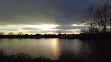 Nehirde gün batımı olan manzara. Bulutların arasından geçen güneş. Güneş ve su ışınları. Akşam yağmurlu manzarası.