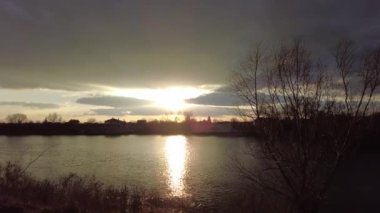 Nehirde gün batımı olan manzara. Bulutların arasından geçen güneş. Güneş ve su ışınları. Akşam yağmurlu manzarası.