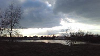 Nehirde gün batımı olan manzara. Bulutların arasından geçen güneş. Güneş ve su ışınları. Akşam yağmurlu manzarası.
