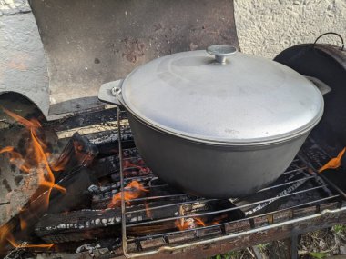 Kırmızı balık çorbasının baharında ateşte pişirmek. Gölün yanındaki ateşte kulağı olan siyah melon şapka. Tahtadan yapılmış bir çorba yalağı. Ateşin üstünde lezzetli balık çorbası