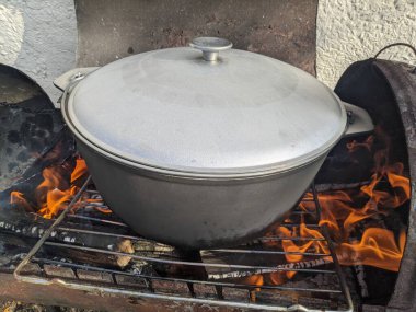 Kırmızı balık çorbasının baharında ateşte pişirmek. Gölün yanındaki ateşte kulağı olan siyah melon şapka. Tahtadan yapılmış bir çorba yalağı. Ateşin üstünde lezzetli balık çorbası