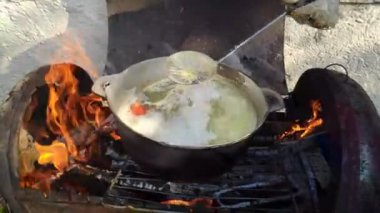 Kırmızı balık çorbasının baharında ateşte pişirmek. Gölün yanındaki ateşte kulağı olan siyah melon şapka. Tahtadan yapılmış bir çorba yalağı. Ateşin üstünde lezzetli balık çorbası