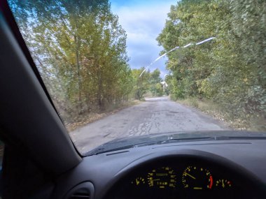 Bulutlu bir havada arabanın içinde. Şoför direksiyonda. Görüş mesafesi zayıf. Ön camda çatlak var..