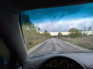 Bulutlu bir havada arabanın içinde. Şoför direksiyonda. Görüş mesafesi zayıf. Ön camda çatlak var..