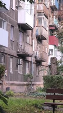 Çok katlı apartmanı, balkonları, ağaçları ve bankı olan şehir avlusu. Beton ve yeşillik karışımı, tipik bir Doğu Avrupa mahallesinde günlük yaşamı yakalıyor..
