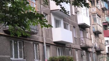 Çok katlı apartmanı, balkonları, ağaçları ve bankı olan şehir avlusu. Beton ve yeşillik karışımı, tipik bir Doğu Avrupa mahallesinde günlük yaşamı yakalıyor..