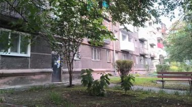 Çok katlı apartmanı, balkonları, ağaçları ve bankı olan şehir avlusu. Beton ve yeşillik karışımı, tipik bir Doğu Avrupa mahallesinde günlük yaşamı yakalıyor..