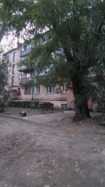 Çok katlı apartmanı, balkonları, ağaçları ve bankı olan şehir avlusu. Beton ve yeşillik karışımı, tipik bir Doğu Avrupa mahallesinde günlük yaşamı yakalıyor..