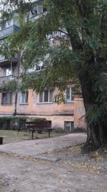 Çok katlı apartmanı, balkonları, ağaçları ve bankı olan şehir avlusu. Beton ve yeşillik karışımı, tipik bir Doğu Avrupa mahallesinde günlük yaşamı yakalıyor..