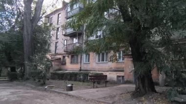 Çok katlı apartmanı, balkonları, ağaçları ve bankı olan şehir avlusu. Beton ve yeşillik karışımı, tipik bir Doğu Avrupa mahallesinde günlük yaşamı yakalıyor..