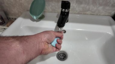 Elde sabun ve musluk suyu. Elinde mavi sabun var. Kadın sabunlu köpüklerle ellerini yıkıyor ve su da yavaş çekimde 4K seçici odaklanıyor. Yavaş çekim videosu.