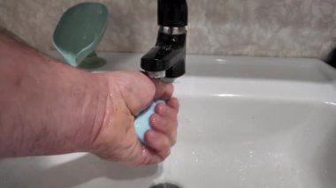 Elde sabun ve musluk suyu. Elinde mavi sabun var. Kadın sabunlu köpüklerle ellerini yıkıyor ve su da yavaş çekimde 4K seçici odaklanıyor. Yavaş çekim videosu.