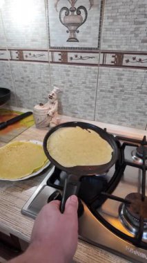 Kızartma tavasında gözleme. Yetenekli aşçı lezzetli krepler pişiriyor, tavada kızartıyor, yakın çekimde yavaş çekimde kırpılıyor. Bir adam evde krep kızartır. Dikey 4K video