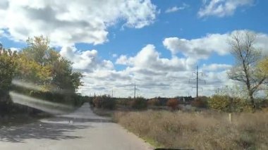 Güneşli bir günde sürücülerin bakış açısı, direksiyonda eller, ileride kırsal yol, ön camdan görünen ağaçlar ve ev. Huzurlu bir yolculuk anı. dikey video