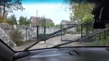 Güneşli bir günde sürücülerin bakış açısı, direksiyonda eller, ileride kırsal yol, ön camdan görünen ağaçlar ve ev. Huzurlu bir yolculuk anı. dikey video