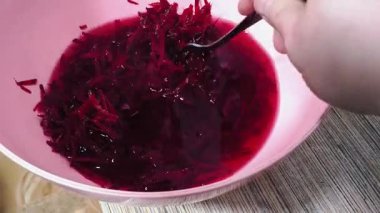 A person is stirring food in a bowl with a fork. Red sweet chopped beets. A person is making a salad. Sweet beets are finely chopped.