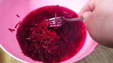A person is stirring food in a bowl with a fork. Red sweet chopped beets. A person is making a salad. Sweet beets are finely chopped.