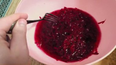 A person is stirring food in a bowl with a fork. Red sweet chopped beets. A person is making a salad. Sweet beets are finely chopped.