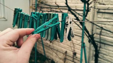 Clothespins on a clothesline. A person opens a clothespin with his fingers. Colorful clothespins hang together on an outdoor clothesline during the rain.