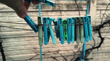 Clothespins on a clothesline. A person opens a clothespin with his fingers. Colorful clothespins hang together on an outdoor clothesline during the rain.
