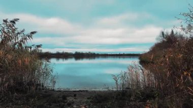 Gölü ve mavi suyu olan güzel bir sonbahar manzarası. Retro-stil manzara. Sıra dışı renkler. Gölde gün batımı. 4K 60fps. Sinematik görüntüler.