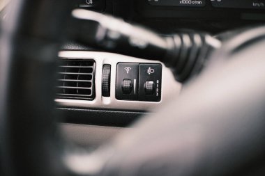 İçinde klima kontrol düğmeleri, gösterge paneli anahtarları, havalandırma delikleri ve elektrikli pencere kontrolleri olan bir arabanın yakın çekim görüntüleri. Detaylı otomotiv bileşenleri tasarım, fonksiyon ve ergonomik gösterir.