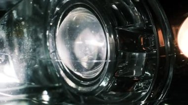 Gece parlak bir şekilde parlayan bir araba farının yakın çekimi yansıtıcı camlar, LED ışınlar ve sinyal aydınlatması sergiliyor. Karanlık bir ortamda dramatik bir otomotiv aydınlatma detayı.