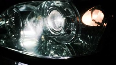 Gece parlak bir şekilde parlayan bir araba farının yakın çekimi yansıtıcı camlar, LED ışınlar ve sinyal aydınlatması sergiliyor. Karanlık bir ortamda dramatik bir otomotiv aydınlatma detayı.