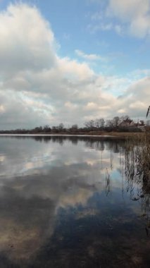 Sakin bir nehrin geniş panoramik manzarası ya da altın kamışlı bir göl dramatik bulutlu bir gökyüzü ve suya yansıyan yumuşak yansımalar. Huzurlu sonbahar sulak arazi, doğal ışık, kırsal manzara.