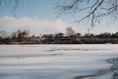 Donmuş göl manzarası, karla kaplı buzlar, sazlıklar ve mavi gökyüzü altındaki kış kıyı şeridi, sakin mevsimsel manzara soğuk havayı, durgun su kenarlarını ve kırsal kış atmosferini gösteriyor..