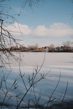 Donmuş göl manzarası, karla kaplı buzlar, sazlıklar ve mavi gökyüzü altındaki kış kıyı şeridi, sakin mevsimsel manzara soğuk havayı, durgun su kenarlarını ve kırsal kış atmosferini gösteriyor..