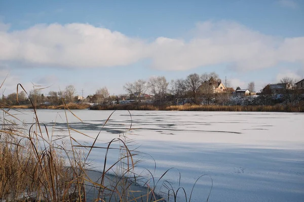 Donmuş göl manzarası, karla kaplı buzlar, sazlıklar ve mavi gökyüzü altındaki kış kıyı şeridi, sakin mevsimsel manzara soğuk havayı, durgun su kenarlarını ve kırsal kış atmosferini gösteriyor..
