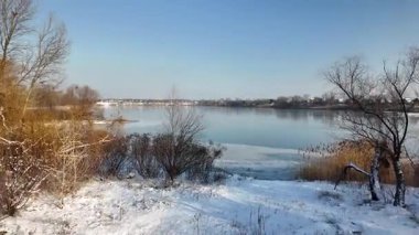 Fotoğrafçının uzun gölgesinin olduğu sakin kış sahnesi el değmemiş karla kaplı zemin, kuru çalılar, temiz mavi gökyüzünün altındaki uzak bir nehre giden yolu çerçeveleyen çıplak ağaçlar. Güneşli soğuk bir gün.