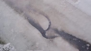 Eriyen karların, kalın beyaz kar katmanlarına, ayak izlerine ve desenli buzlu kenarlara işlenmiş eriyen su kanallarının soyut görüntüsü. Huzurlu kış buzları.