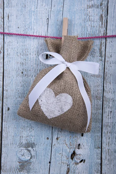 Burlap pouch hanging on clothesline on old wooden background — Stock Photo, Image