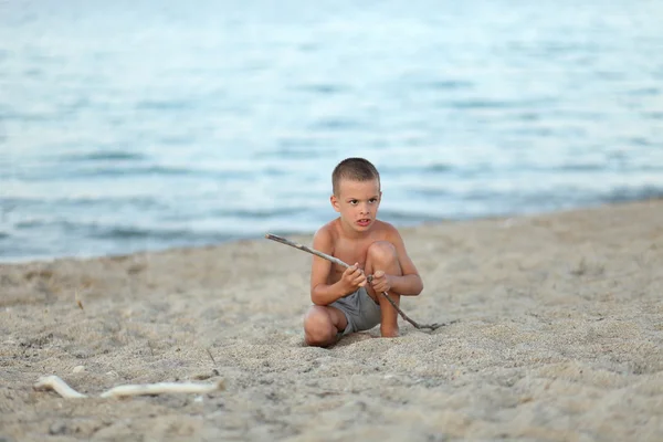 Boy spela med pinne på stranden alon — Stockfoto