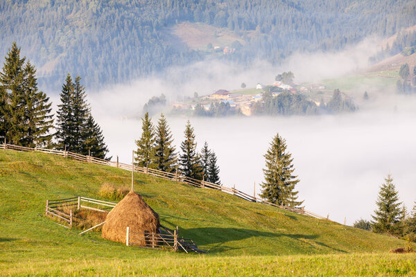 Amazing scenery of idyllic countryside with rolling hills veiled in morning fog. Aerial view of a hilltop farmhouse on a foggy spring morning