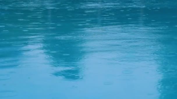 Ondulações em uma lagoa feita por gotas de chuva sobre a superfície lisa da água azul azur — Vídeo de Stock
