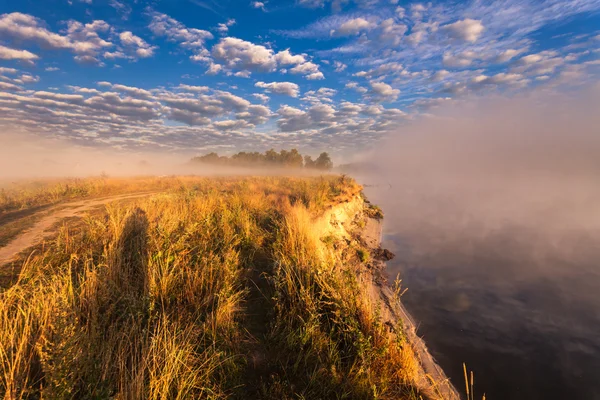 Mistige ochtend op de rivier en de wolken weerspiegeld in water — Stockfoto