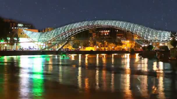 Tbilisi, Grúzia - 2015. július 29.: Éjszakai kilátás a fényesen kivilágított hidak, a béke. A híd nyúlik és folyó, és összeköti a régi Tbiliszi területei — Stock videók