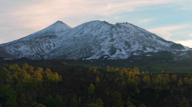 Karla kaplı dağ ve ormanın üzerinde gün doğumu, ağaçların arasından parlayan güneşe doğru uçan hava aracı, sıcak. Teide. Tenerife. İspanya