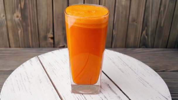 Carrot juice into glass  rotating, wood background. Seamless Loop — Stock Video