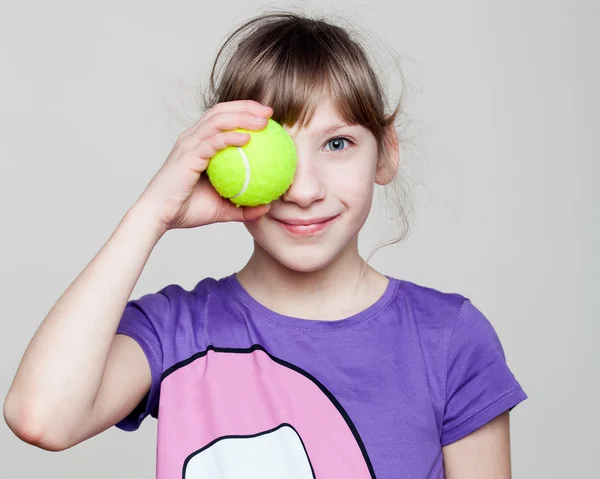 Porträtt av en söt flicka som håller en tennisboll vid ögat — Stockfoto