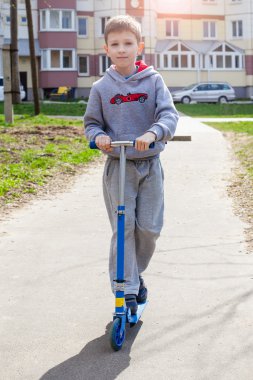 Küçük çocuk sokakta scooter kullanıyor.