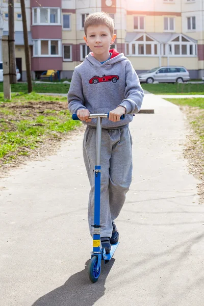 Küçük çocuk sokakta scooter kullanıyor.