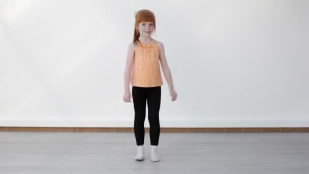 Little red-haired girl performing cross twinel exercise after a junp — Stock Video
