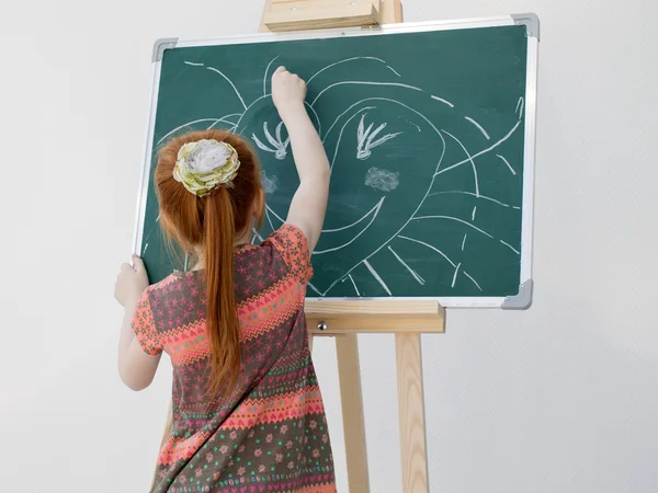 La niña pelirroja dibuja en una pizarra escolar — Foto de Stock