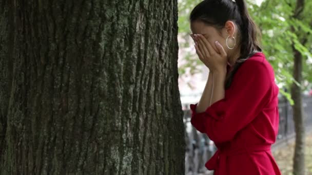 Mädchen im roten Kleid weint in der Nähe eines Baumes — Stockvideo